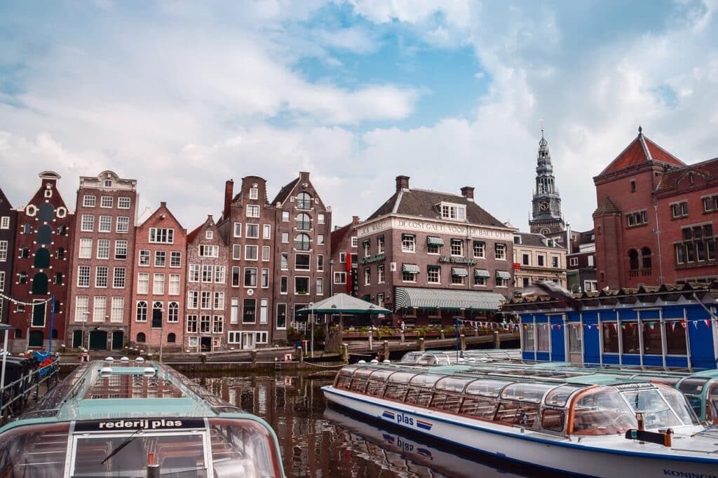 Date ideeën in Amsterdam 3 Een gracht in Amsterdam met rondvaartboten met glazen daken aangemeerd voor traditionele Nederlandse gebouwen - een ideale partner om de smalle gevels, zadeldaken en de kerktoren die oprijst onder een gedeeltelijk bewolkte hemel te verkennen.