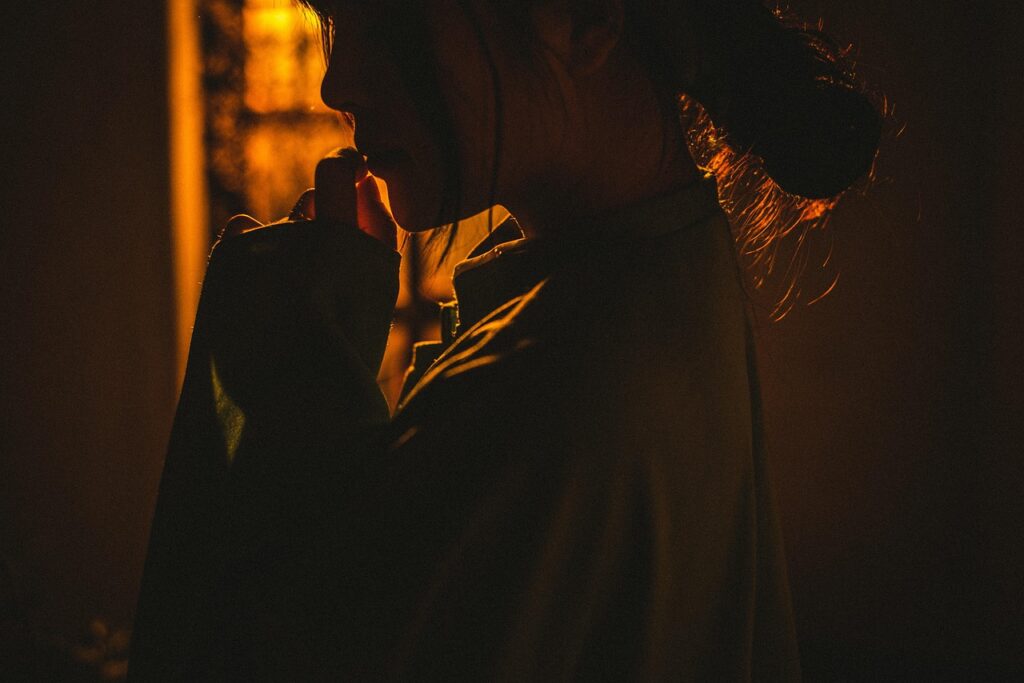 Onzeker in een relatie 1 Een persoon in een los gewaad wordt getoond in warm, laag licht met het gezicht meestal in de schaduw, de hand naar de mond brengend en onzeker in een relatie lijkend - nadenkend of contemplatief.