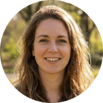 Een vrouw met lang, golvend bruin haar glimlacht naar buiten. Ze draagt een neutraal topje en staat in natuurlijk zonlicht, met groene bomen en onscherp gebladerte op de achtergrond. Het cirkelvormige beeld legt perfect vast hoe ze geniet van het Aanbod van de natuur.