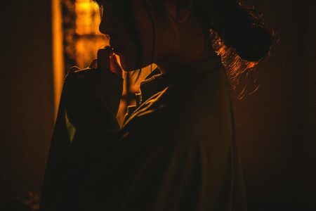 Een persoon in een los gewaad wordt getoond in warm, laag licht met het gezicht meestal in de schaduw, de hand naar de mond brengend en onzeker in een relatie lijkend - nadenkend of contemplatief.