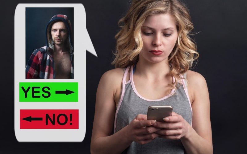 Een vrouw met blond haar kijkt naar haar telefoon, naast een groot scherm waarop een man in een shirt met capuchon te zien is en opties als "JA" of "NEE!", die lijken op een datingapp waar ze haar ideale partner zoekt.